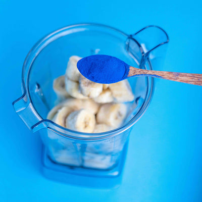 Spoonful of blue powder over a blender with ingredients on a blue background