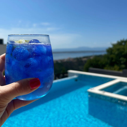 Blue spirulina ice cubes in a glass by the pool – vibrant natural blue drink coloring