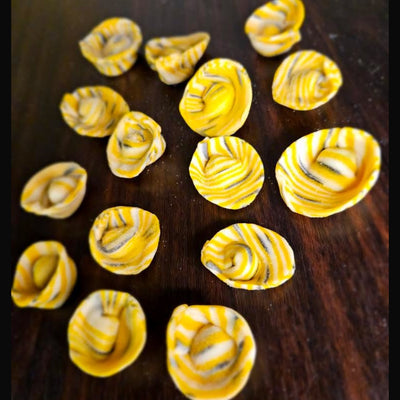 Yellow, black and white striped pasta shells on a dark wooden surface