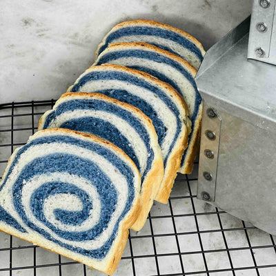 Sliced brioche bread colored with butterfly pea powder, showing natural blue spiral pattern in the dough